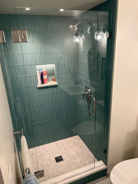 Walk-in shower with green vertical tile, niche and glass door